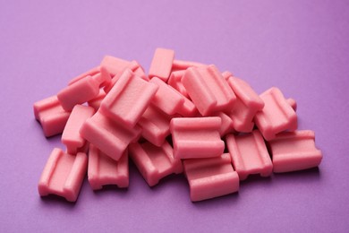 Photo of Tasty pink chewing gums on purple background, closeup