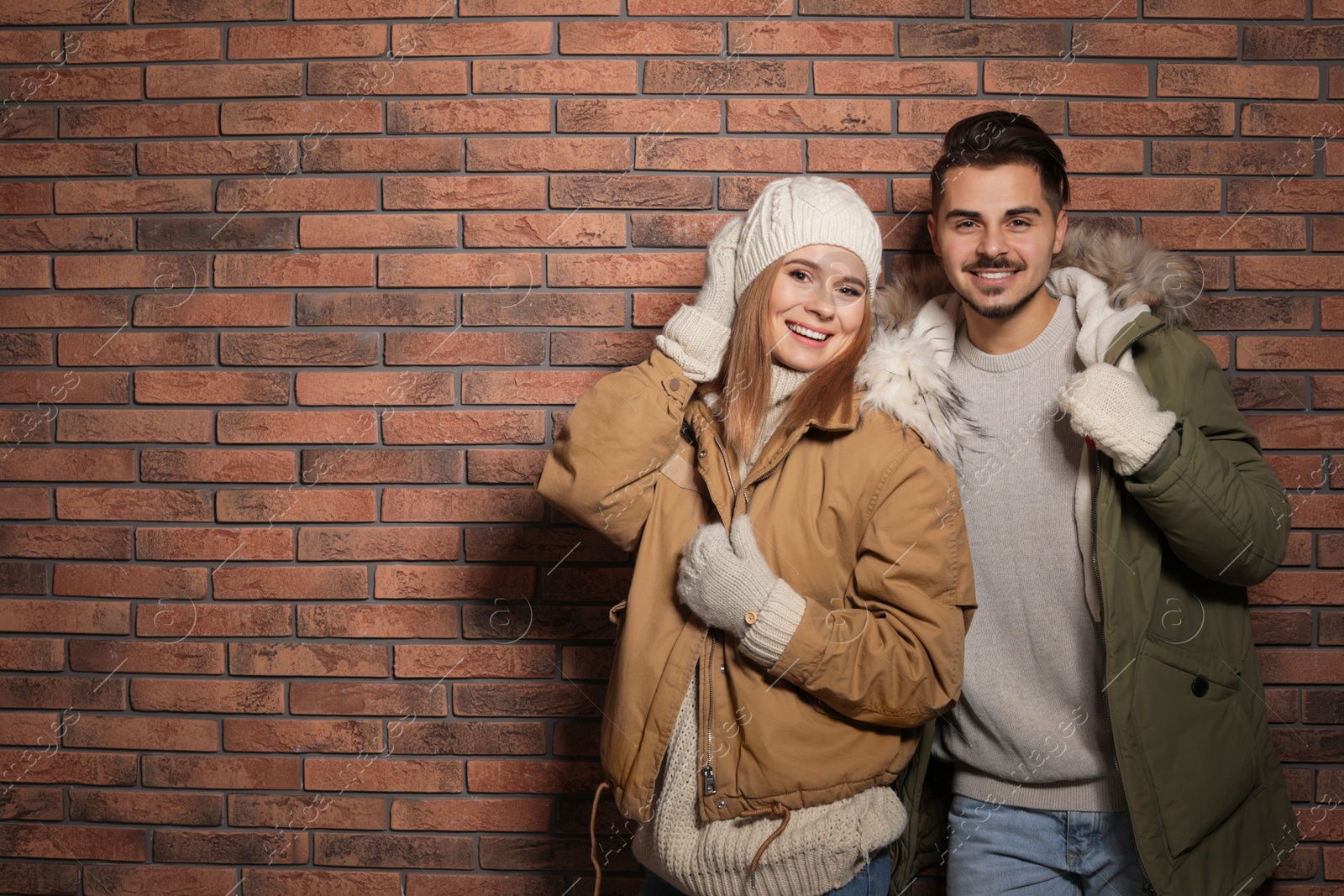 Photo of Young couple wearing warm clothes against brick wall, space for text. Ready for winter vacation