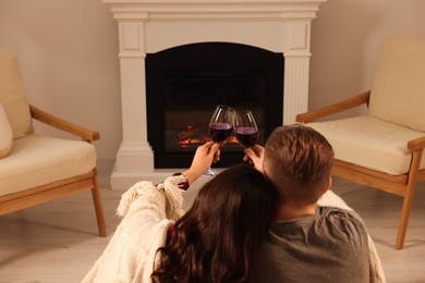 Photo of Lovely couple with glasses of wine resting together near fireplace at home, back view