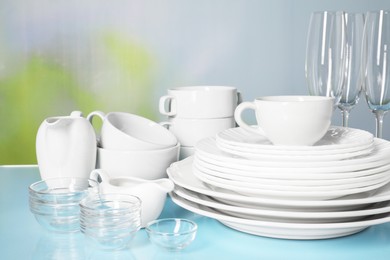 Photo of Set of clean dishes and glasses on light blue table