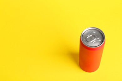 Photo of Energy drink in orange can on yellow background, space for text