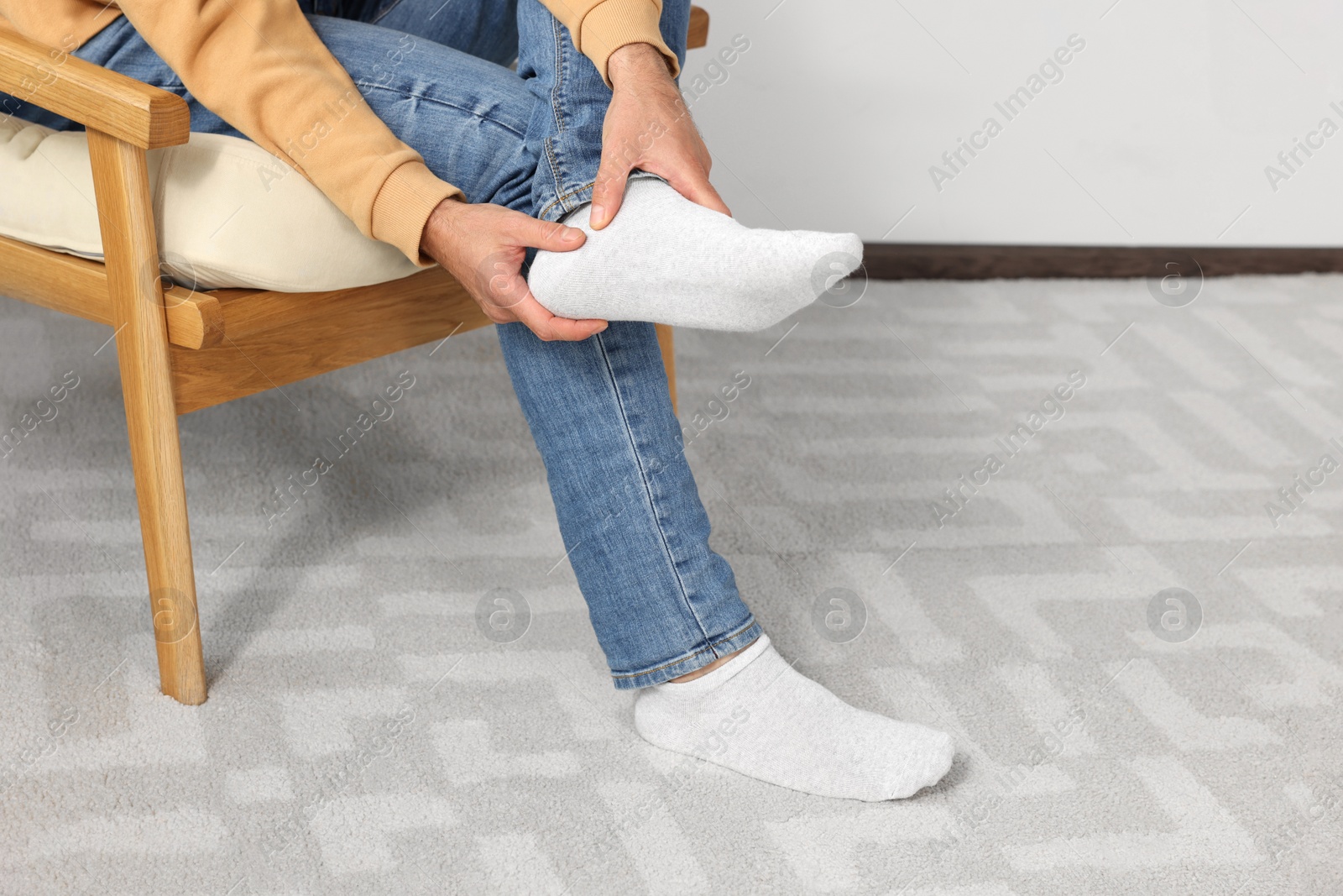 Photo of Man suffering from leg pain and touching heel on soft armchair indoors, closeup