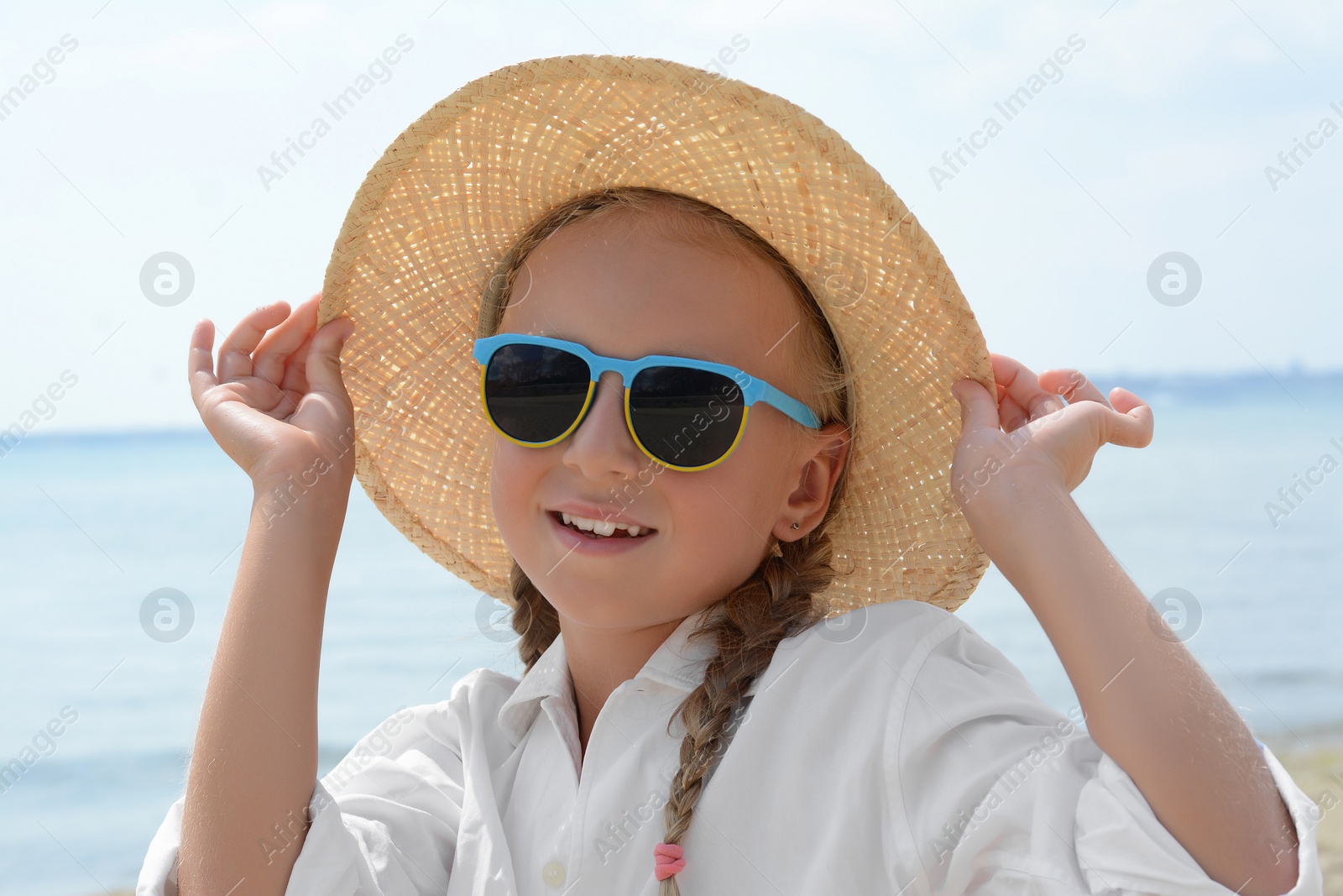 Photo of Little girl wearing sunglasses and hat at beach on sunny day