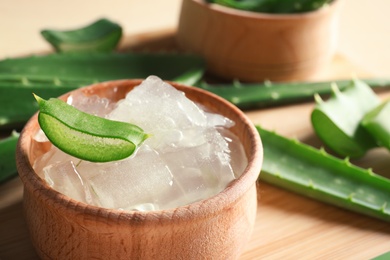 Photo of Bowl with peeled aloe vera and green leaves on wooden board