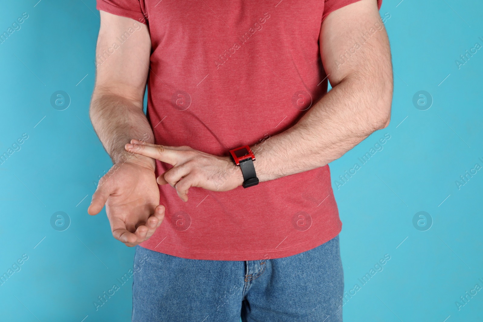 Photo of Young man checking pulse on color background, closeup
