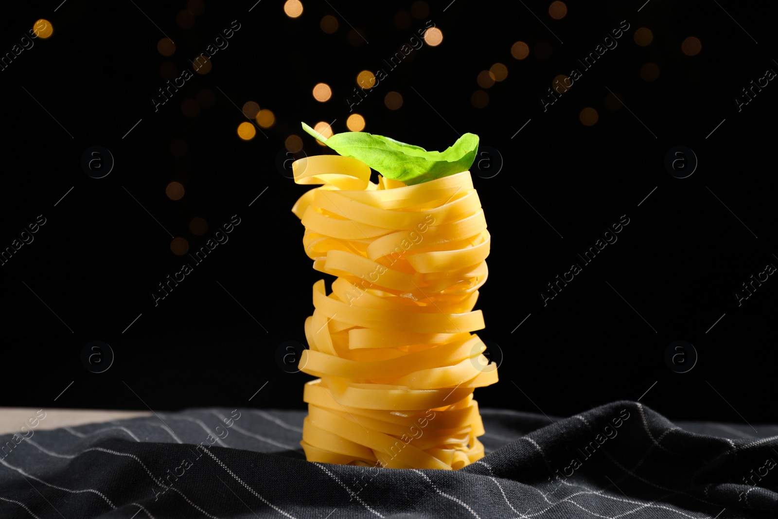 Photo of Uncooked tagliatelle pasta on fabric against blurred lights