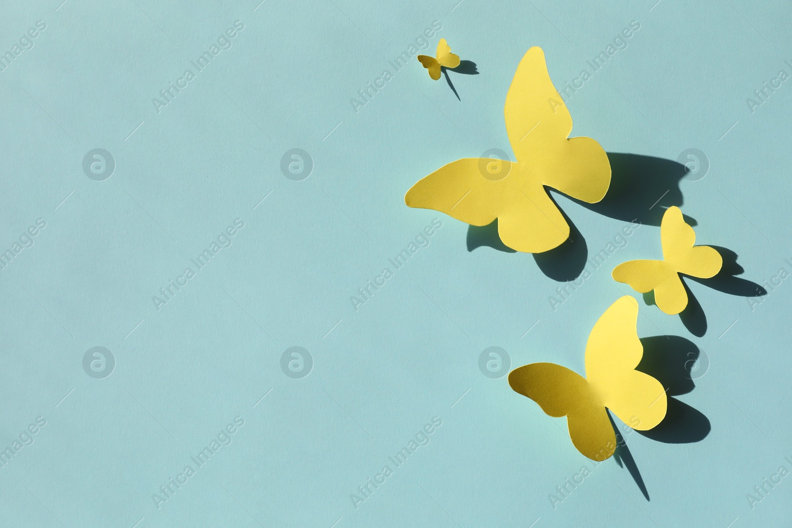 Photo of Yellow paper butterflies on turquoise background, top view. Space for text