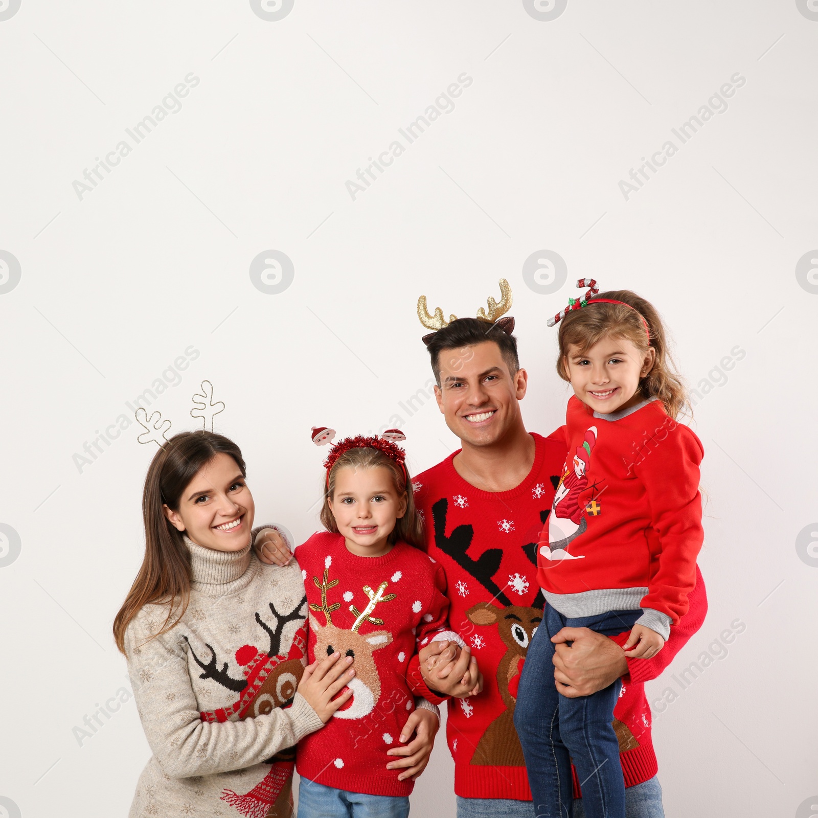 Photo of Family in Christmas sweaters and festive headbands on white background