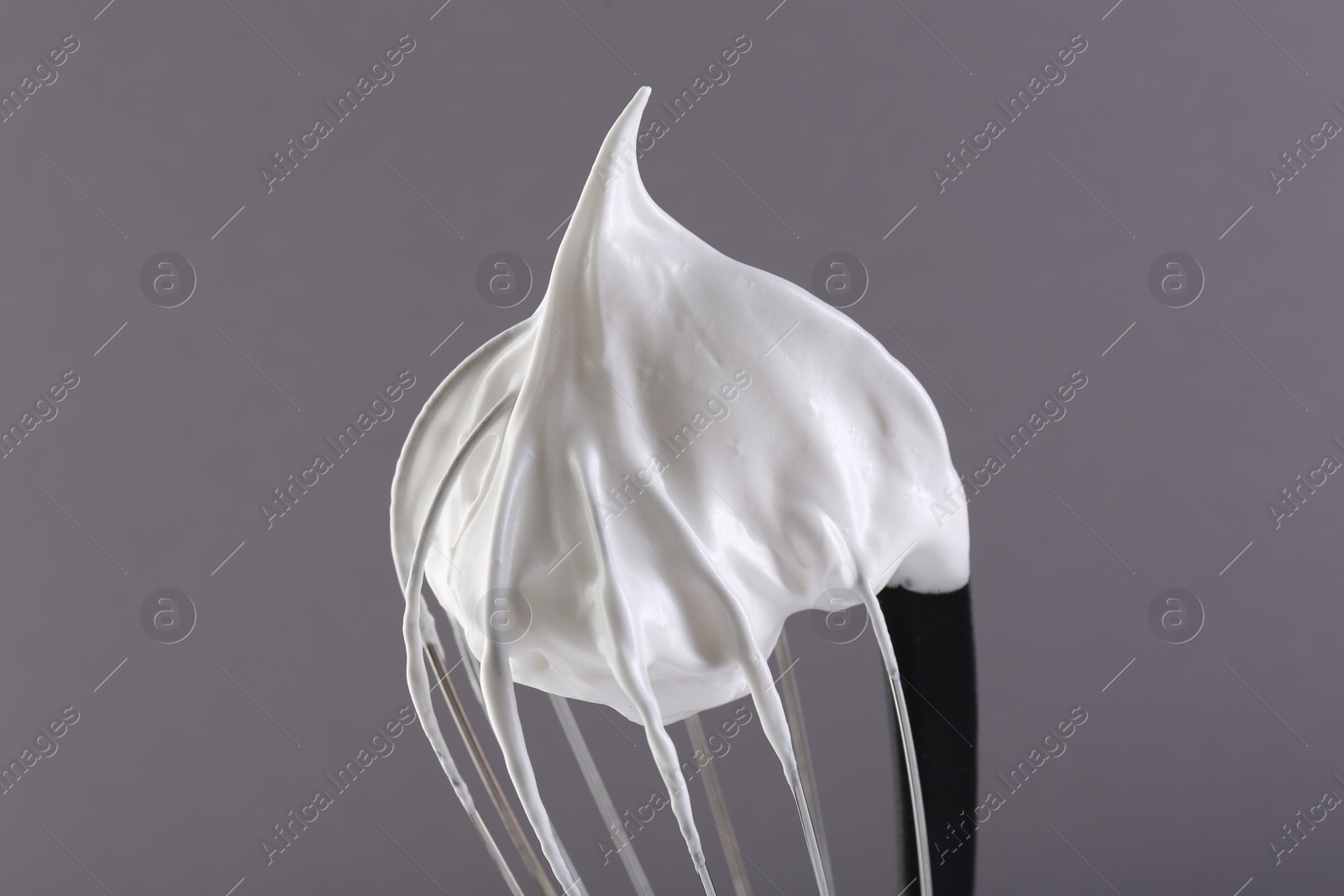 Photo of Whisk with whipped cream on grey background, closeup