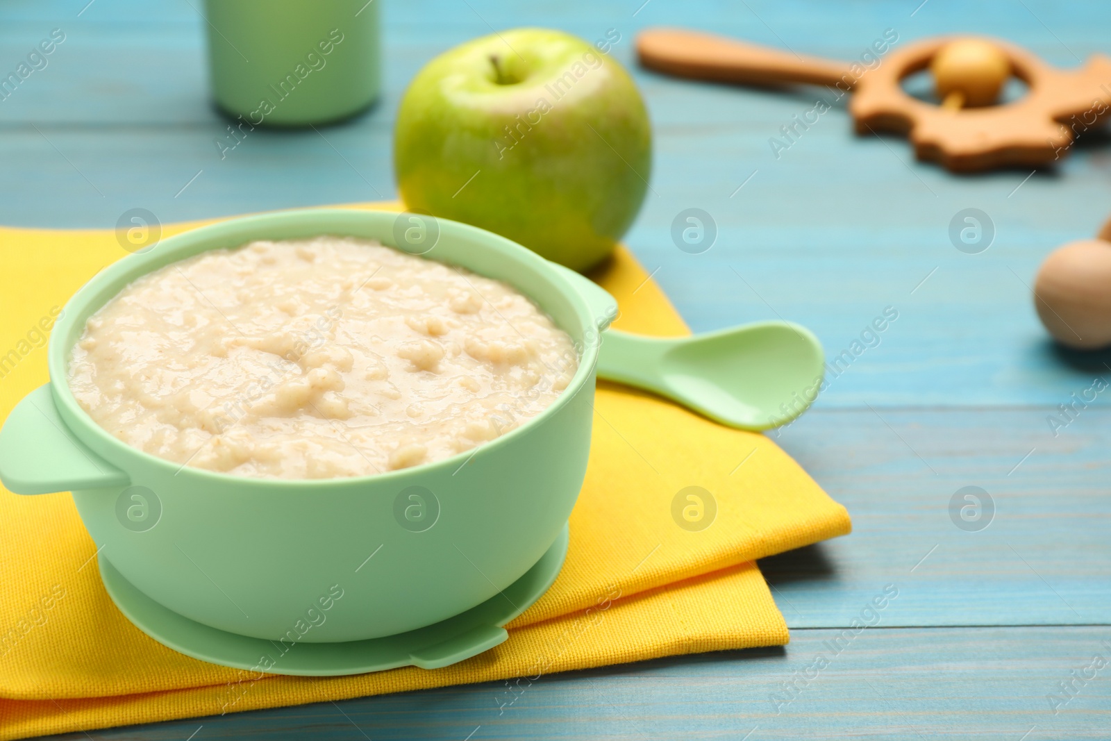 Photo of Plastic dishware with healthy baby food on light blue wooden background, closeup. Space for text