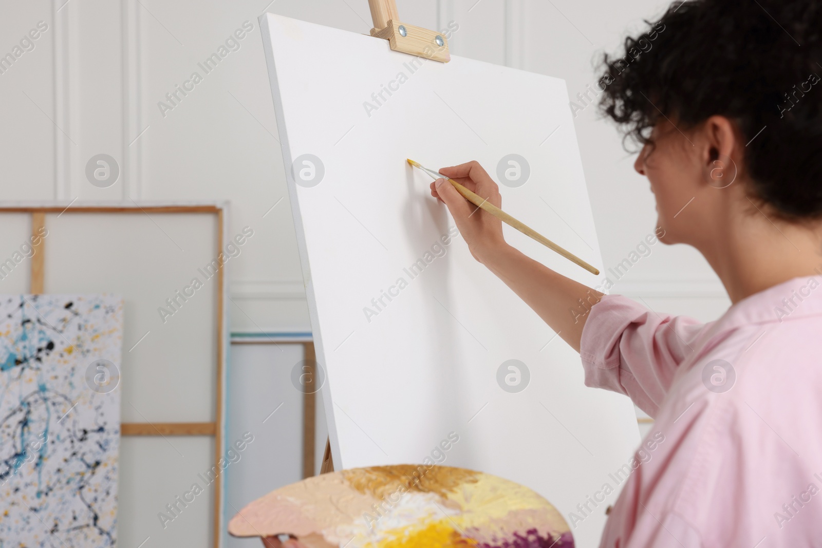 Photo of Young woman painting on easel with canvas in studio