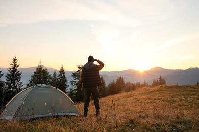 Man near camping tent in mountains at sunset, back view