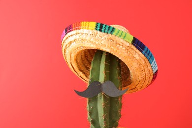 Photo of Cactus with Mexican sombrero hat and fake mustache on red background