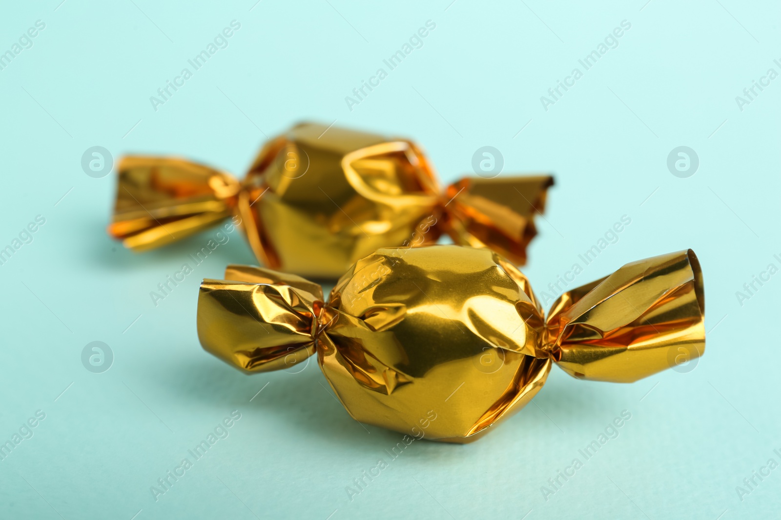 Photo of Candies in golden wrappers on light blue background, closeup