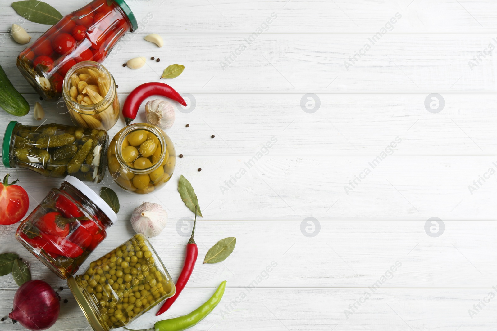 Photo of Glass jars with different pickled vegetables on white wooden background, flat lay. Space for text