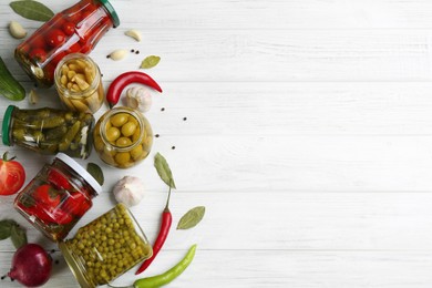 Glass jars with different pickled vegetables on white wooden background, flat lay. Space for text