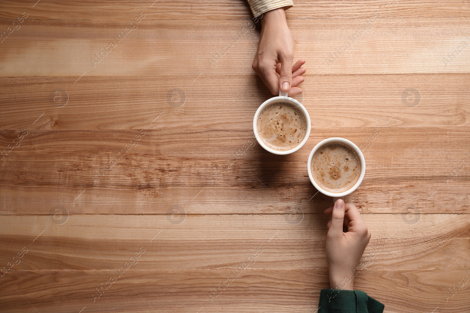 Photo of Women with cups of coffee at wooden table, top view. Space for text