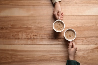 Photo of Women with cups of coffee at wooden table, top view. Space for text