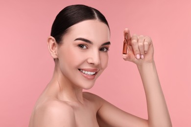 Photo of Beautiful young woman holding skincare ampoule on pink background