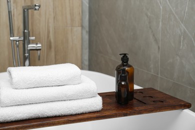 Photo of Stacked bath towels and personal care products on tub tray in bathroom