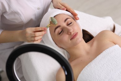 Cosmetologist making face massage with roller to client in clinic, top view