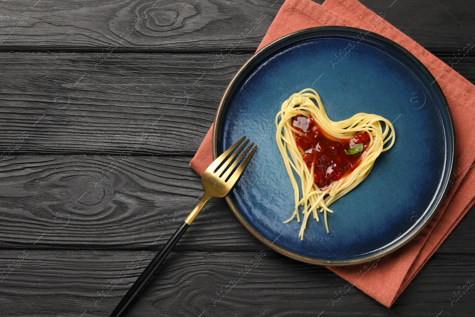 Photo of Heart made with spaghetti and sauce on black wooden table, top view. Space for text
