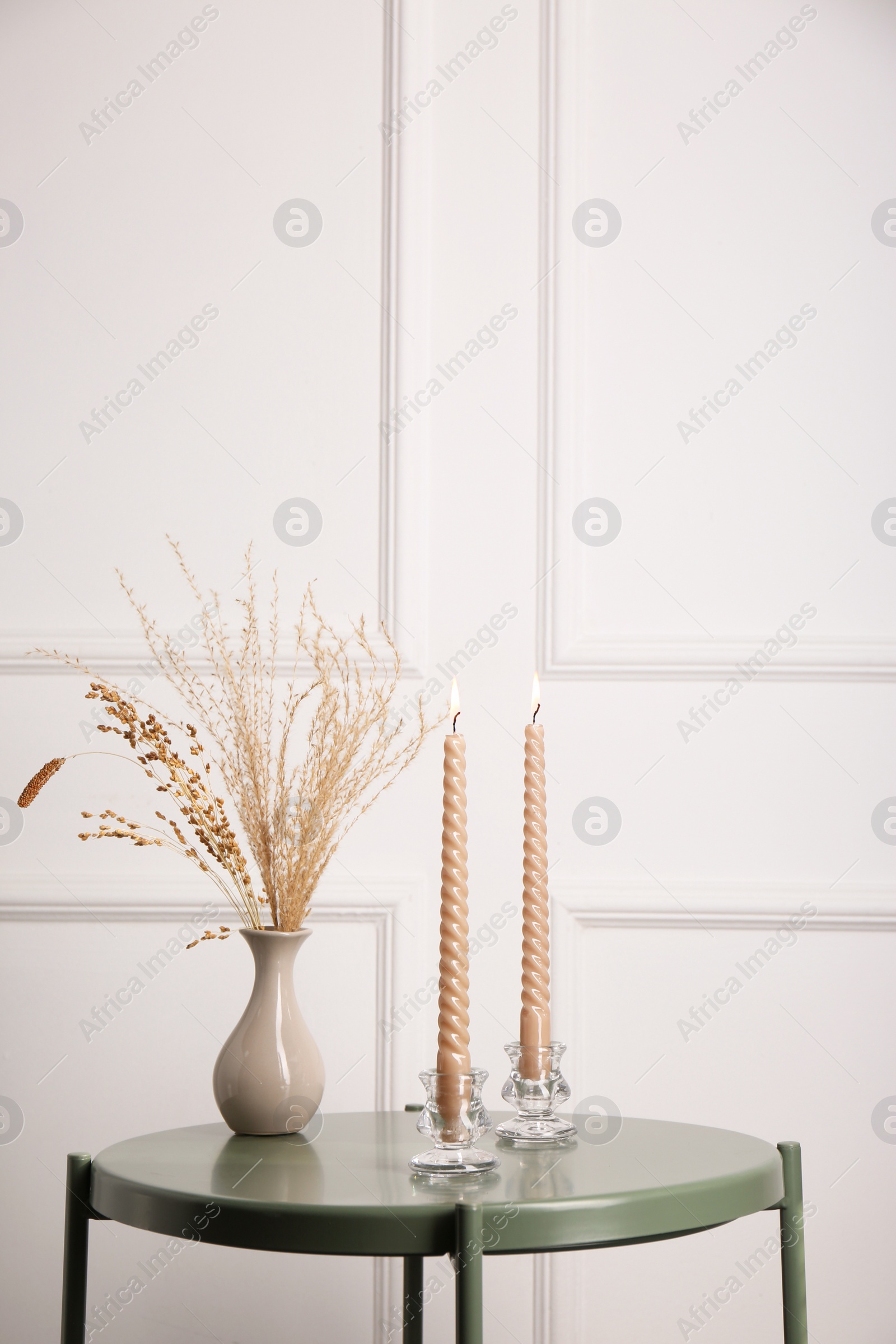 Photo of Dry plants in vase and burning candles on table near white wall