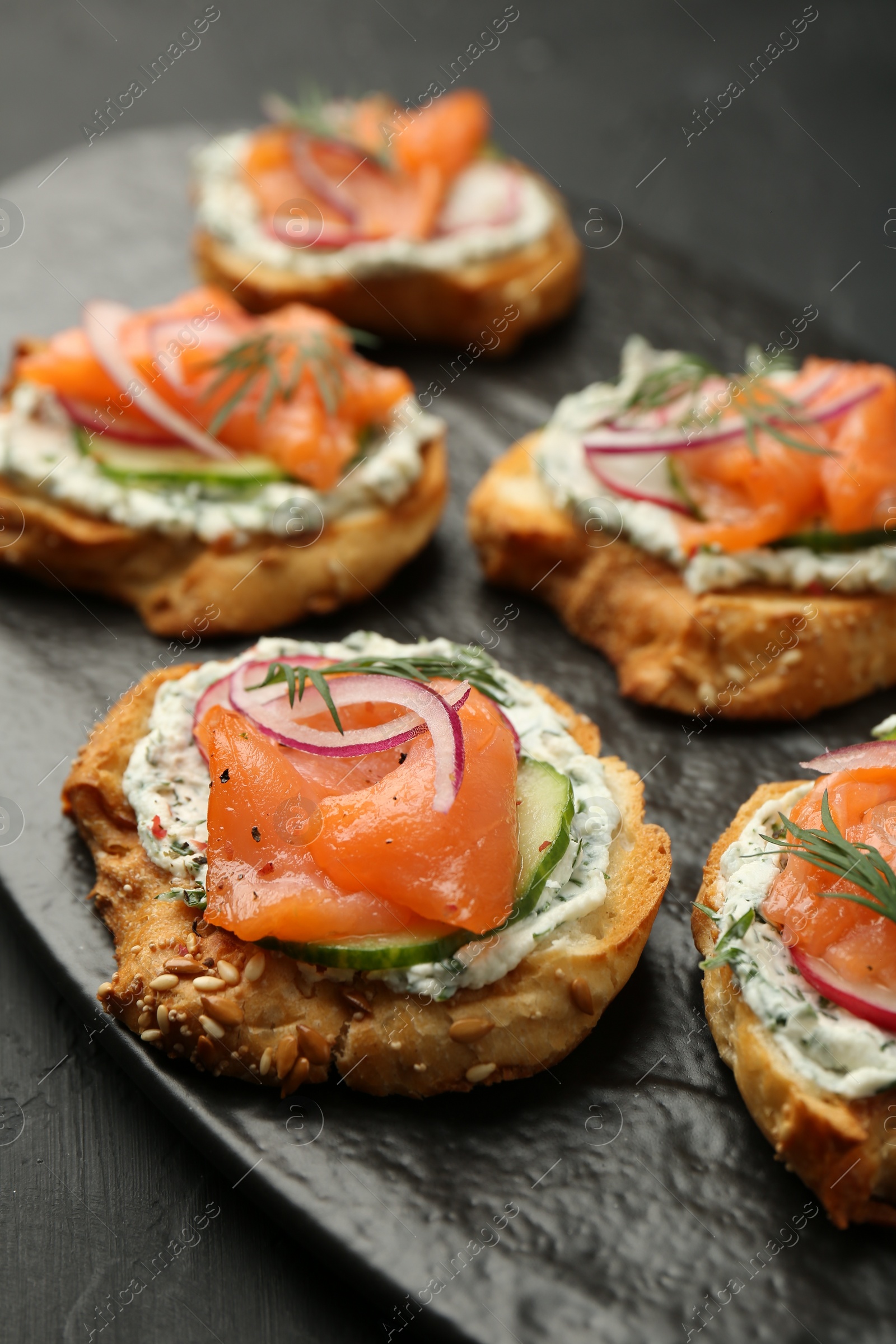 Photo of Tasty canapes with salmon, cucumber, radish and cream cheese on black table, closeup