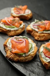 Photo of Tasty canapes with salmon, cucumber, radish and cream cheese on black table, closeup