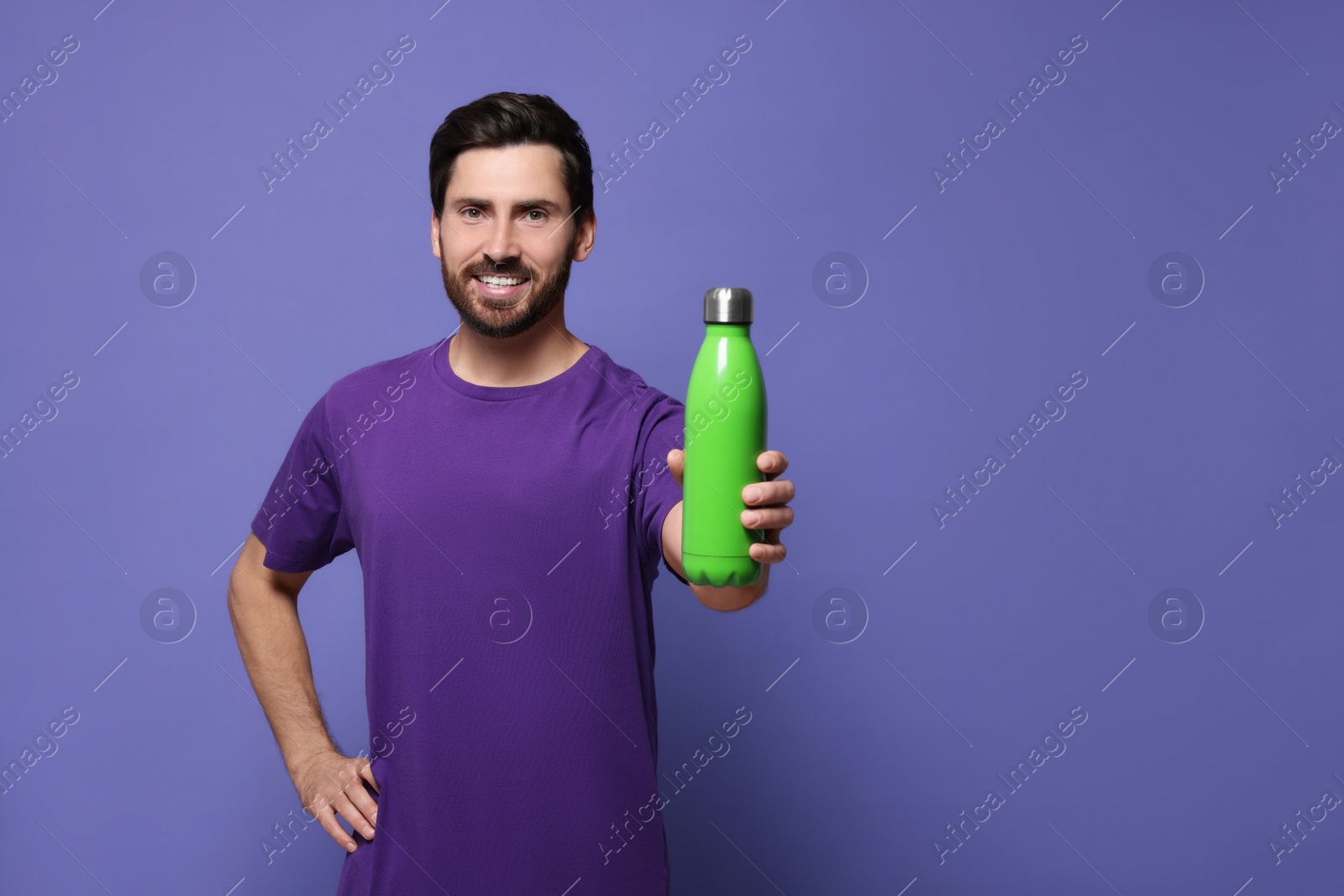 Photo of Man with green thermo bottle on violet background. Space for text