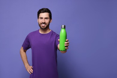 Man with green thermo bottle on violet background. Space for text