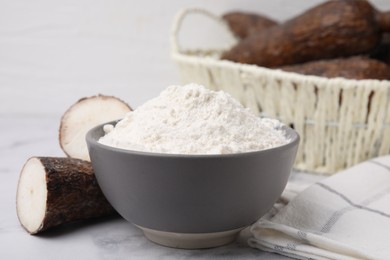 Photo of Bowl with cassava flour and roots on white marble table