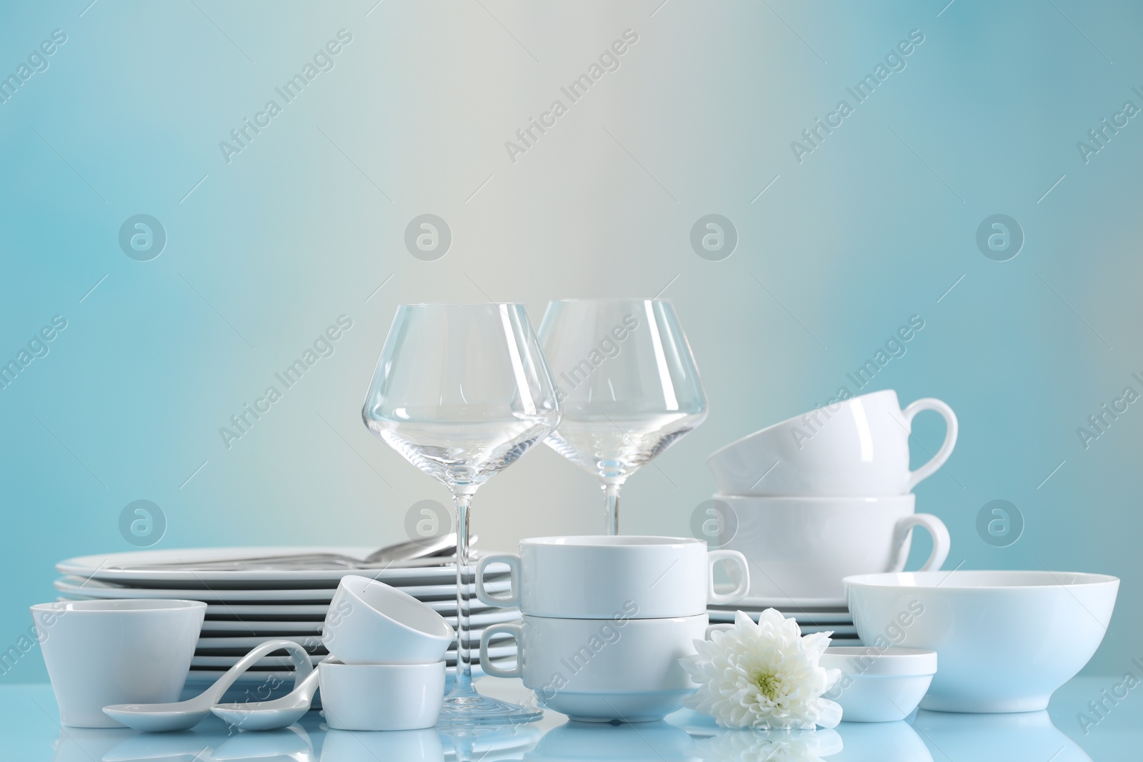 Photo of Set of many clean dishware, flower and glasses on light blue table