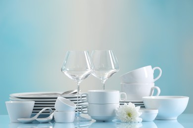 Photo of Set of many clean dishware, flower and glasses on light blue table