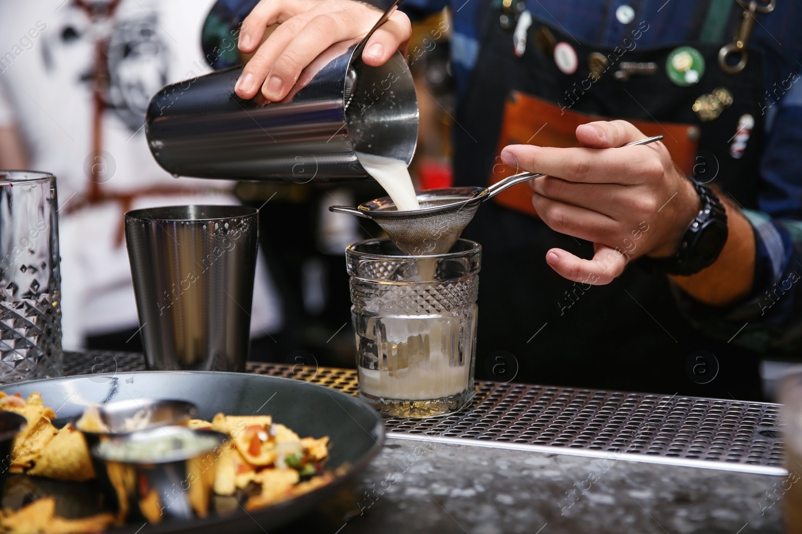 Photo of Bartender pouring tasty cocktail at counter in nightclub, closeup