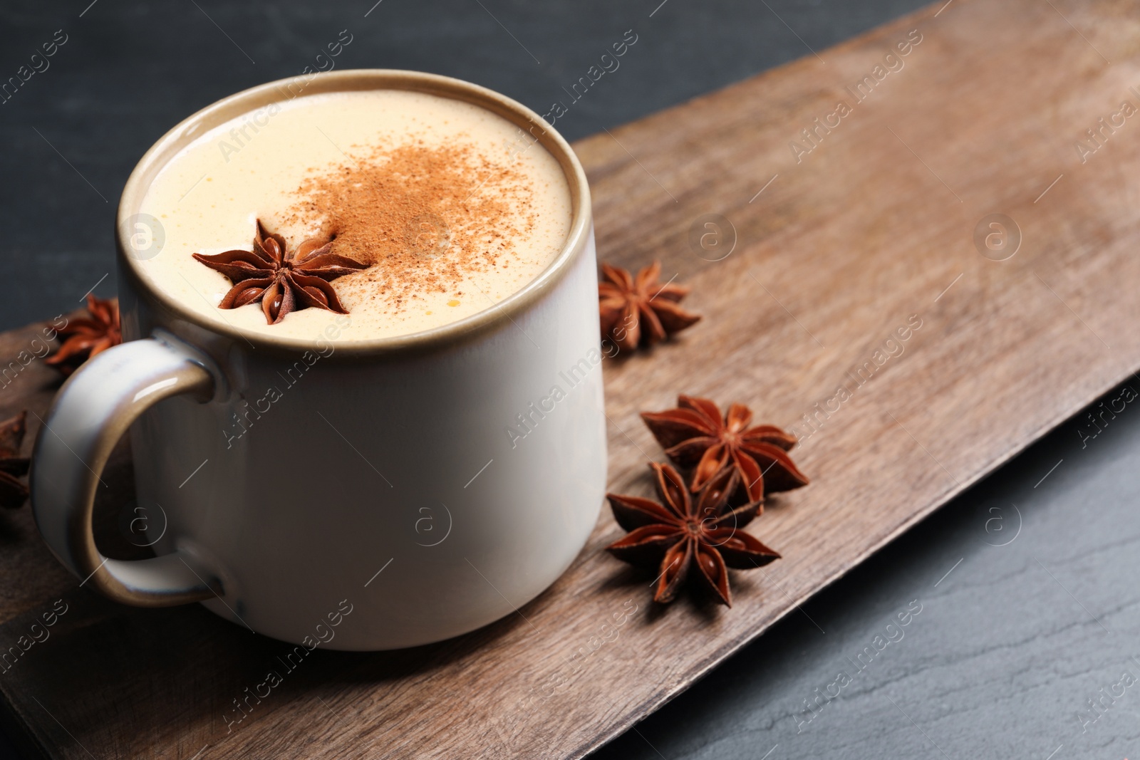 Photo of Delicious eggnog with anise and cinnamon on black table, closeup. Space for text