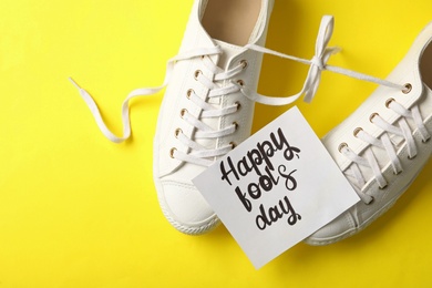 Photo of Shoes with tied laces and Happy Fools' Day note on yellow background, flat lay
