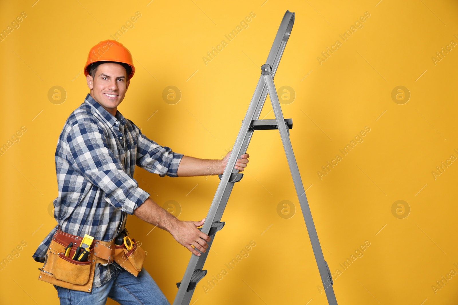 Photo of Professional builder climbing up metal ladder on yellow background
