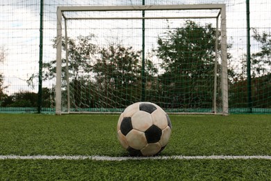 Dirty soccer ball on green football field against net