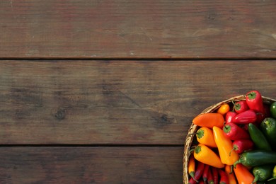 Photo of Wicker basket with many different fresh chilli peppers on wooden table, top view. Space for text