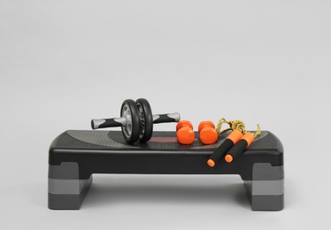 Photo of Step platform, skipping rope, dumbbells and abdominal wheel on light background, space for text. Sport equipment