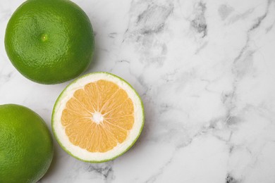 Photo of Whole and cut sweetie fruits on white marble table, flat lay. Space for text