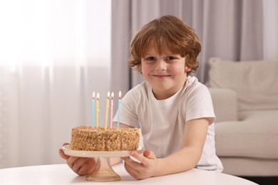 Photo of Cute boy with birthday cake at table indoors