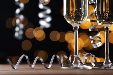 Photo of Glasses of champagne and serpentine streamers against black background with blurred lights, closeup. Space for text