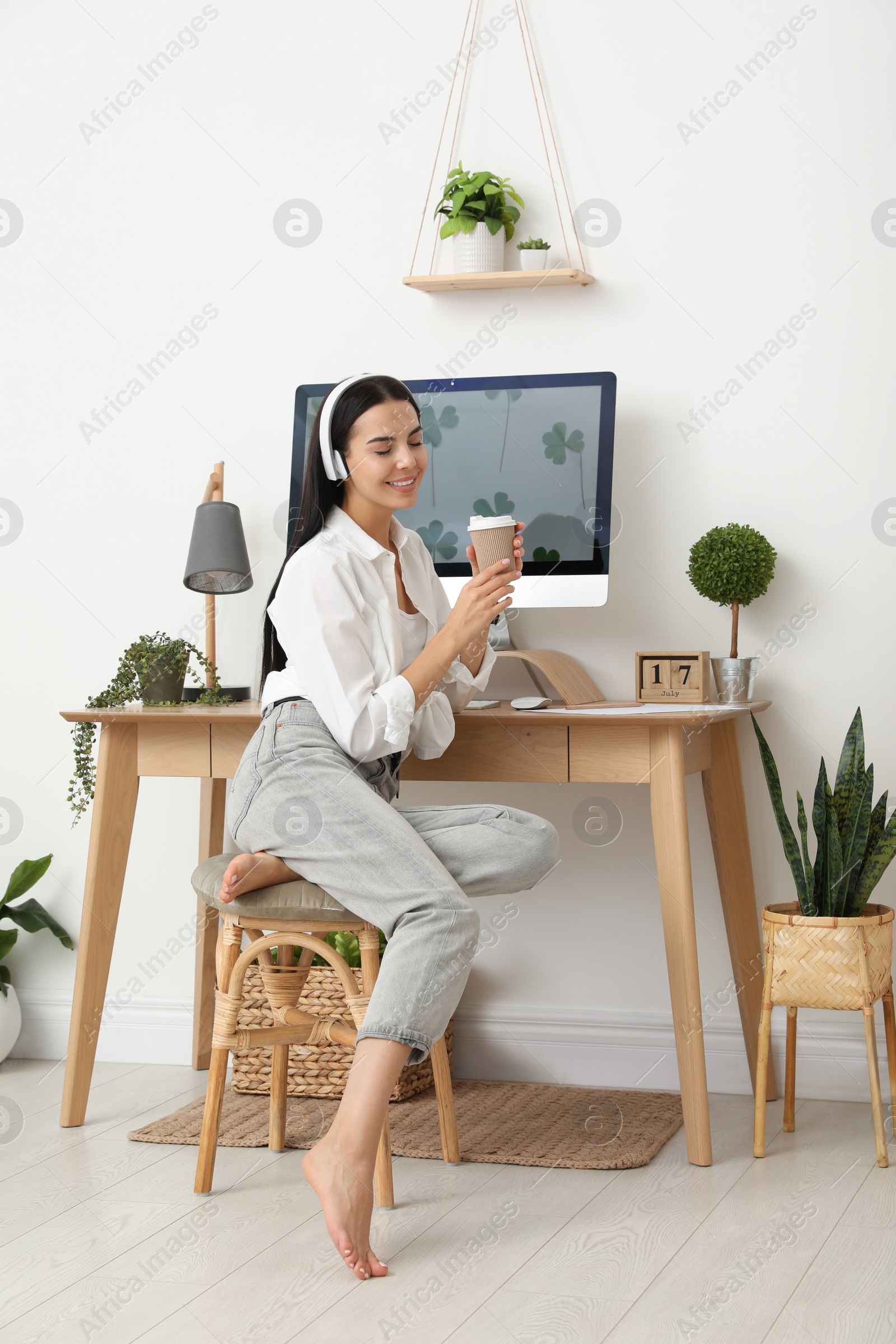 Photo of Young woman with cup of drink at table in room. Home office