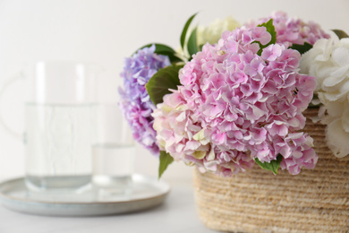 Beautiful hydrangea flowers in basket on light table, closeup