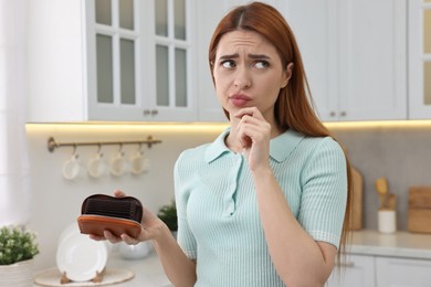 Confused woman with empty wallet at home