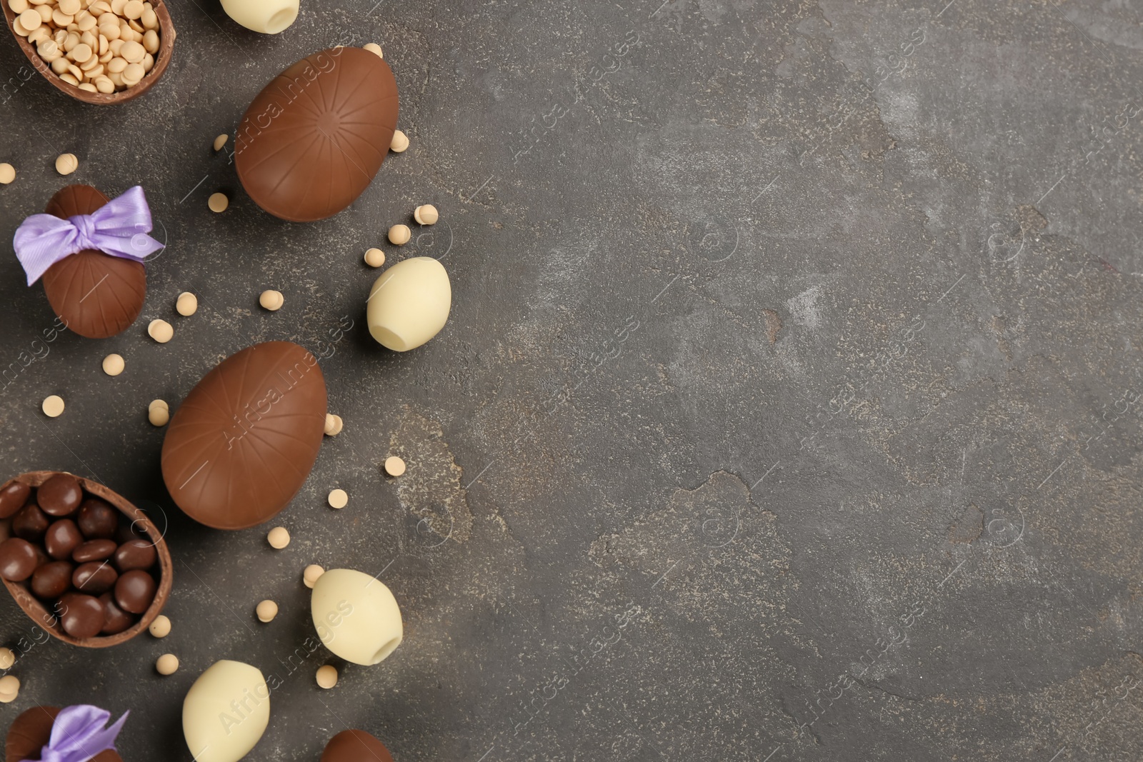 Photo of Sweet chocolate eggs and candies on grey table, flat lay. Space for text