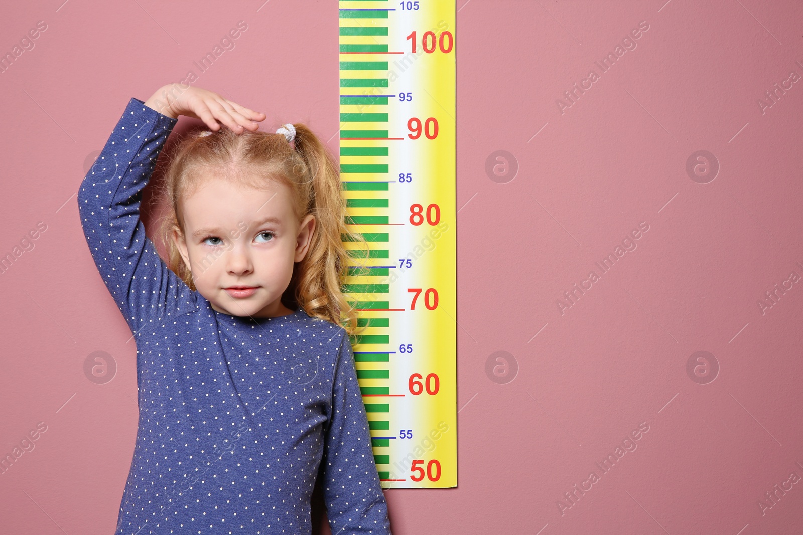 Photo of Little girl measuring her height on color background