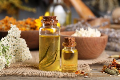 Bottles of essential oils and different herbs on wooden table